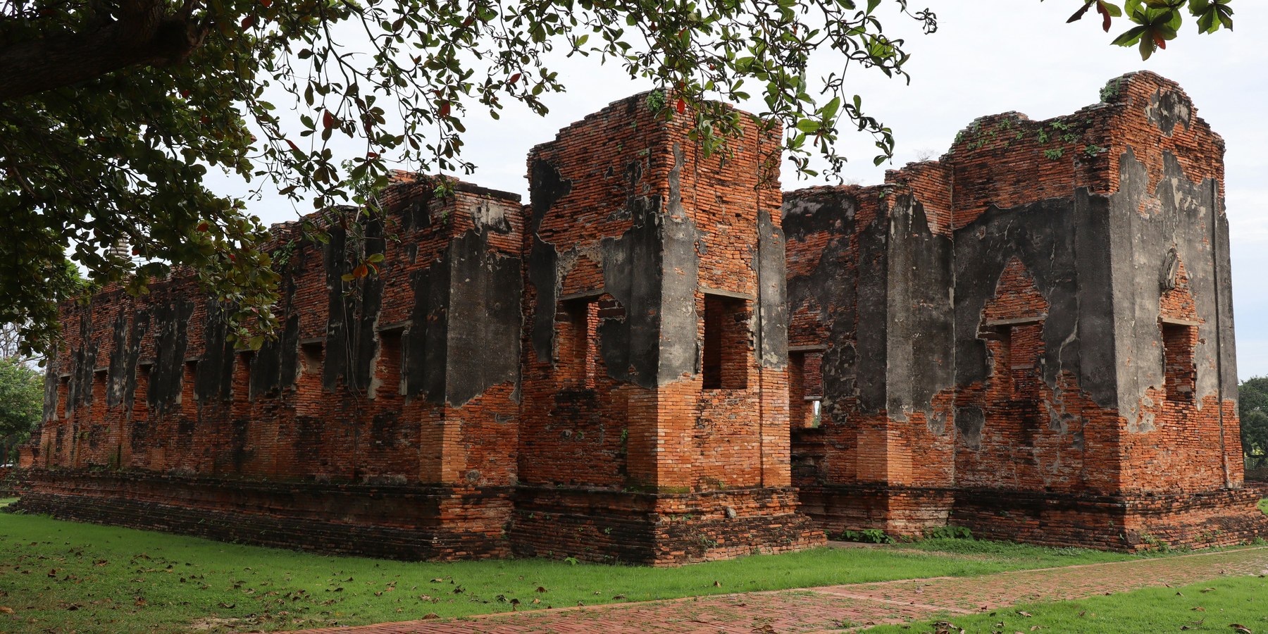 Historic red-brick temple ruins in Ayutthaya, framed by tree branches.