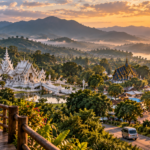 Panoramic sunrise view over Chiang Rai with the White Temple, Blue Temple, golden Clock Tower and forested mountains