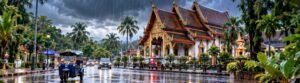 Rain falling on a Thai-inspired street with a temple and local transport