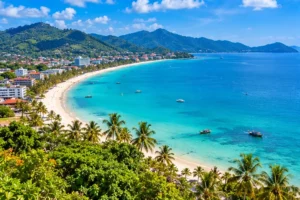 Illustration of a broad Phuket-style west-coast bay with beachfront buildings and green hills